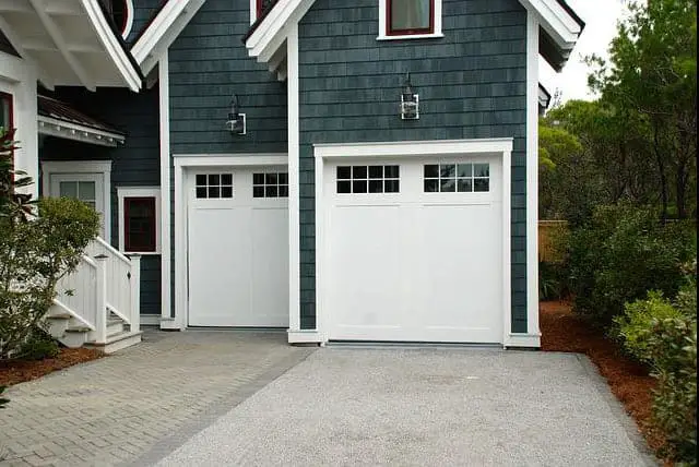 two small white garage doors with windows on blue house